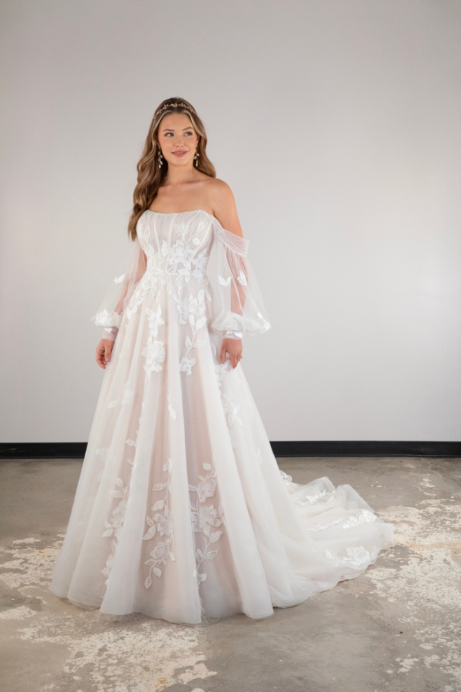 model is wearing an off the shoulder wedding dress with a long train