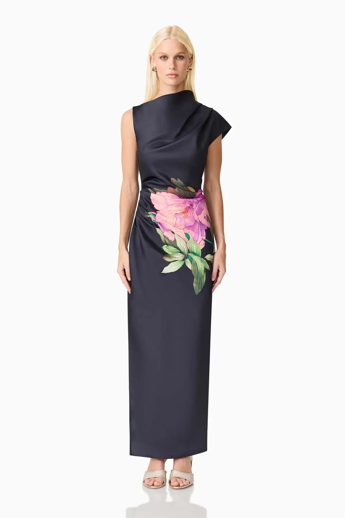 Model is wearing a glossy duchess satin gown with an asymmetrical neckline, thigh-high slit, and pink floral accents that add drama and romance.