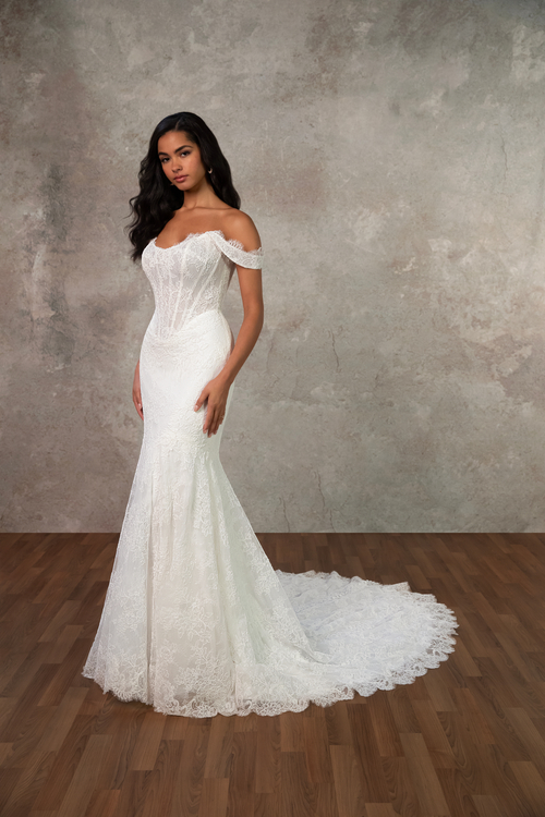 A woman wearing an elegant, off-the-shoulder white wedding dress with a fitted bodice and a flowing train, standing against a textured gray background.