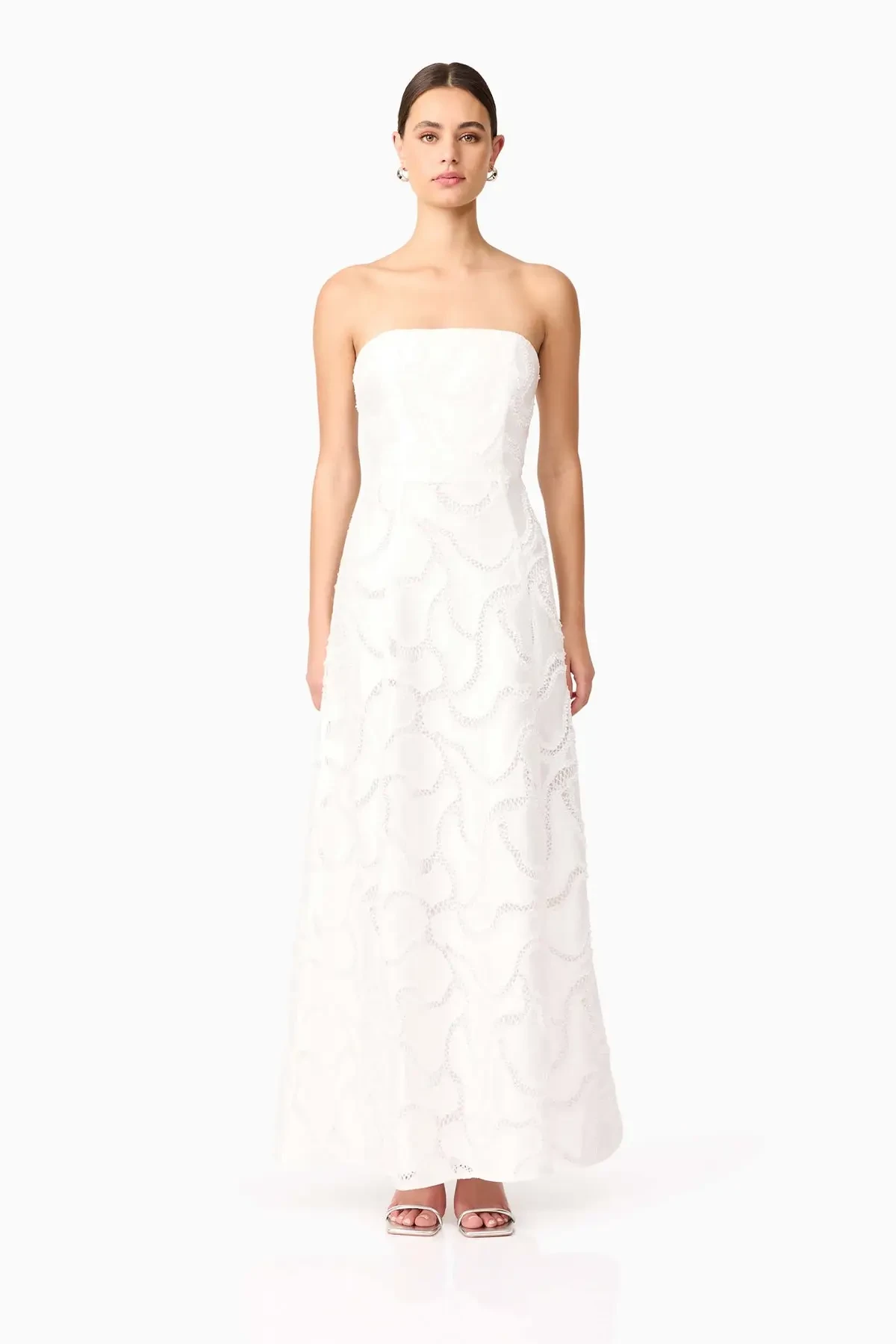 Model is wearing a strapless white gown in beaded sateen fabric that shimmers subtly, finished with a timeless fit-and-flare silhouette.