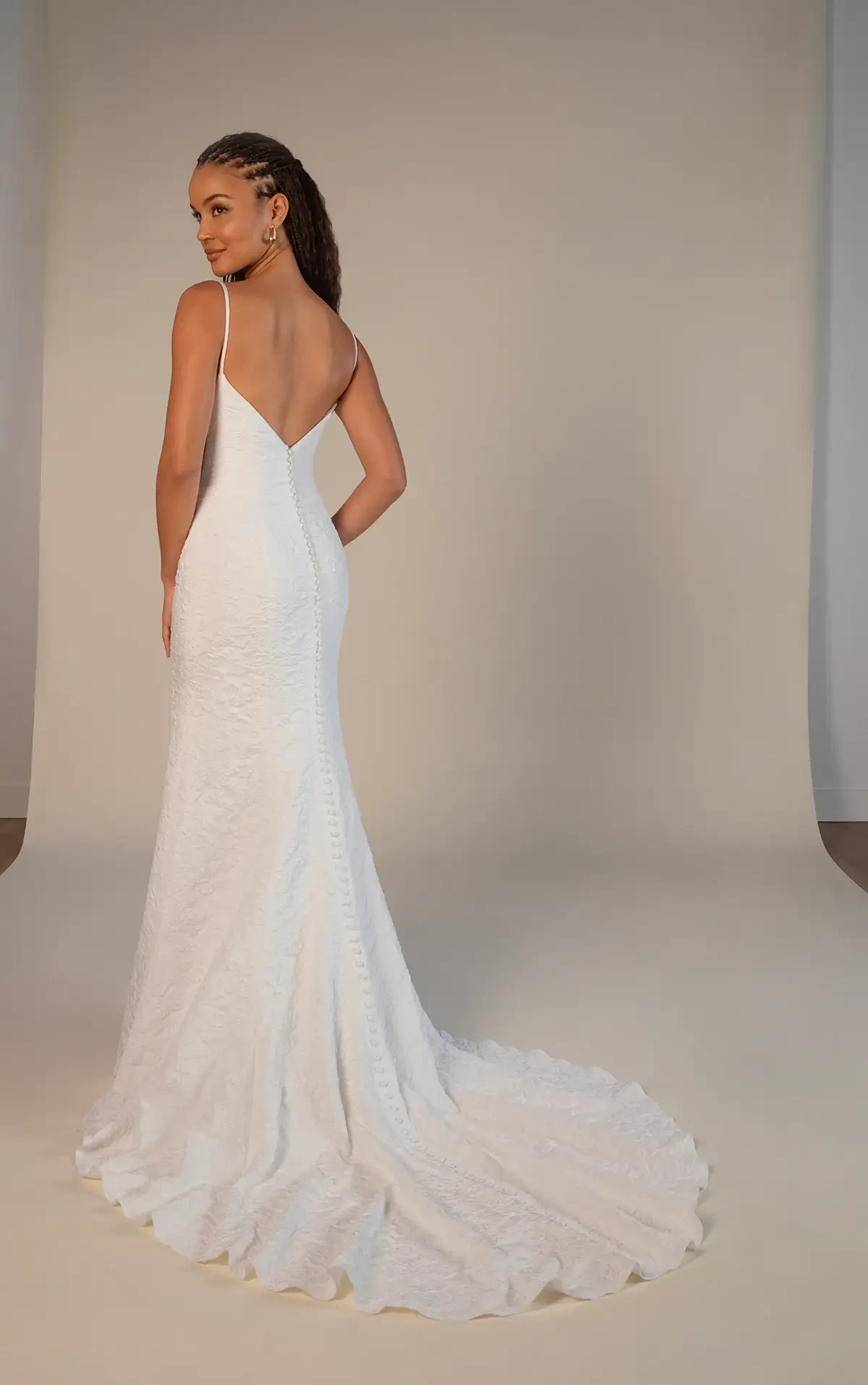 Model is wearing a satin jacquard gown with spaghetti straps, a square neckline, side cutouts, and a row of buttons down the back.