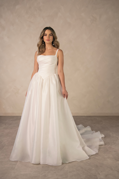 A woman wearing a elegant white wedding dress, standing against a neutral background.
