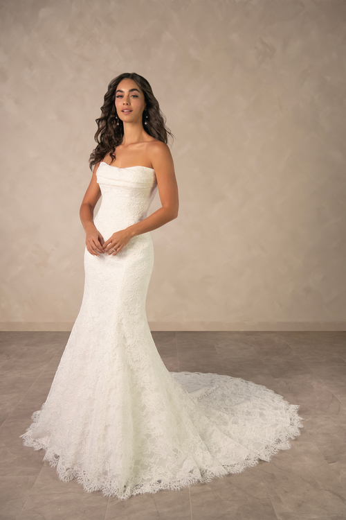 A woman in a strapless white wedding dress standing elegantly against a neutral background.