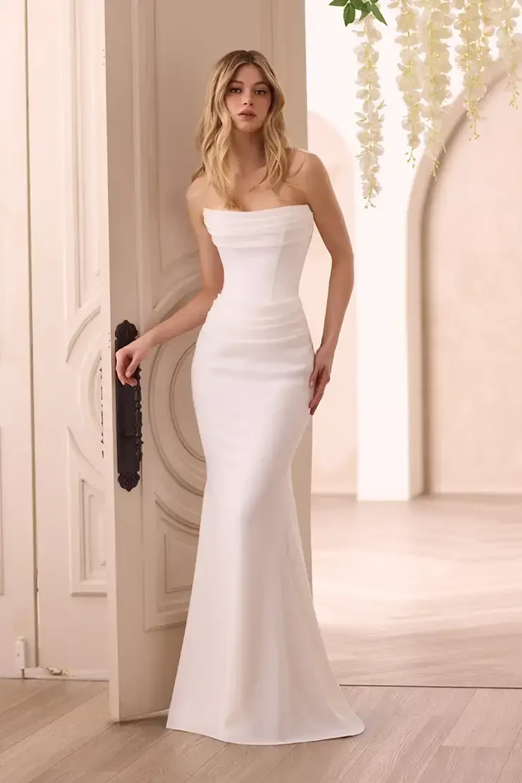 A woman in a strapless white gown standing elegantly beside a door with floral decor.